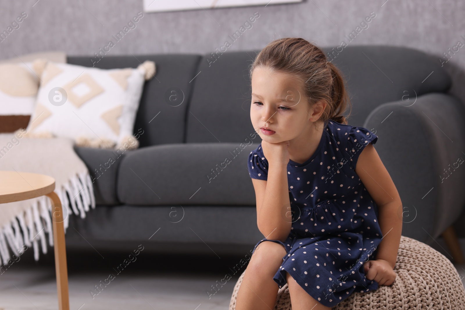 Photo of Resentful little girl sitting on pouf at home, space for text