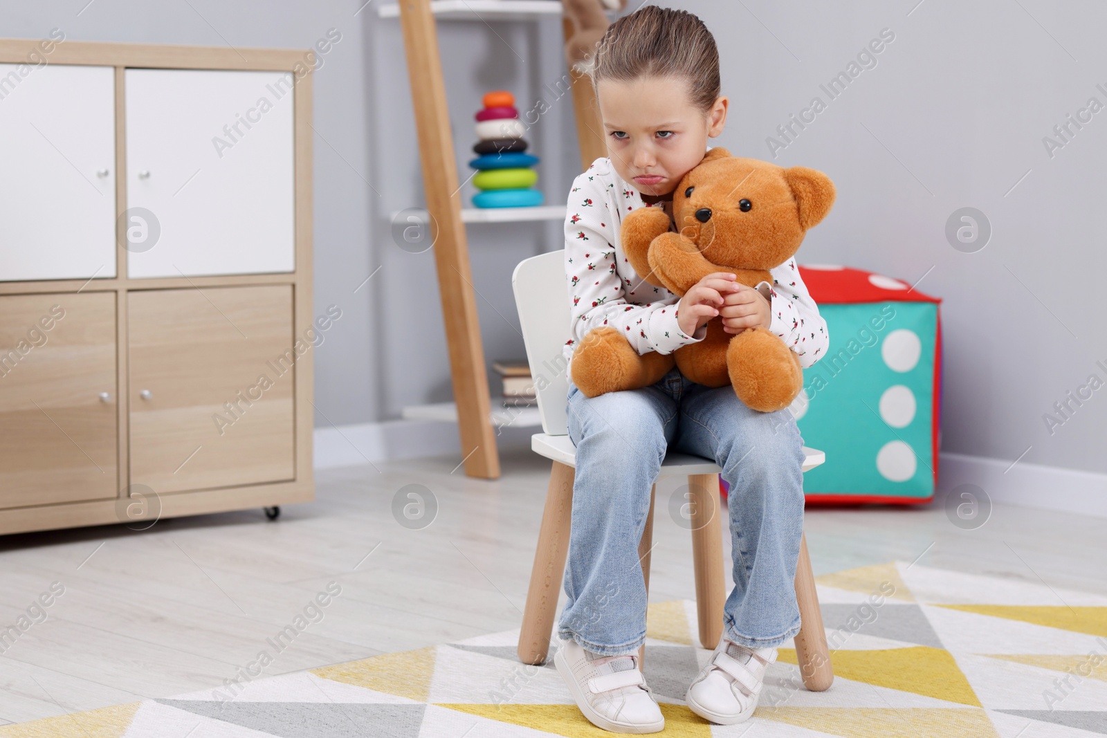 Photo of Resentful little girl with teddy bear at home, space for text