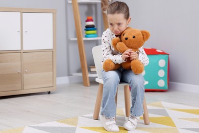 Photo of Resentful little girl with teddy bear at home, space for text