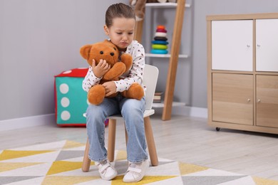 Photo of Resentful little girl with teddy bear at home