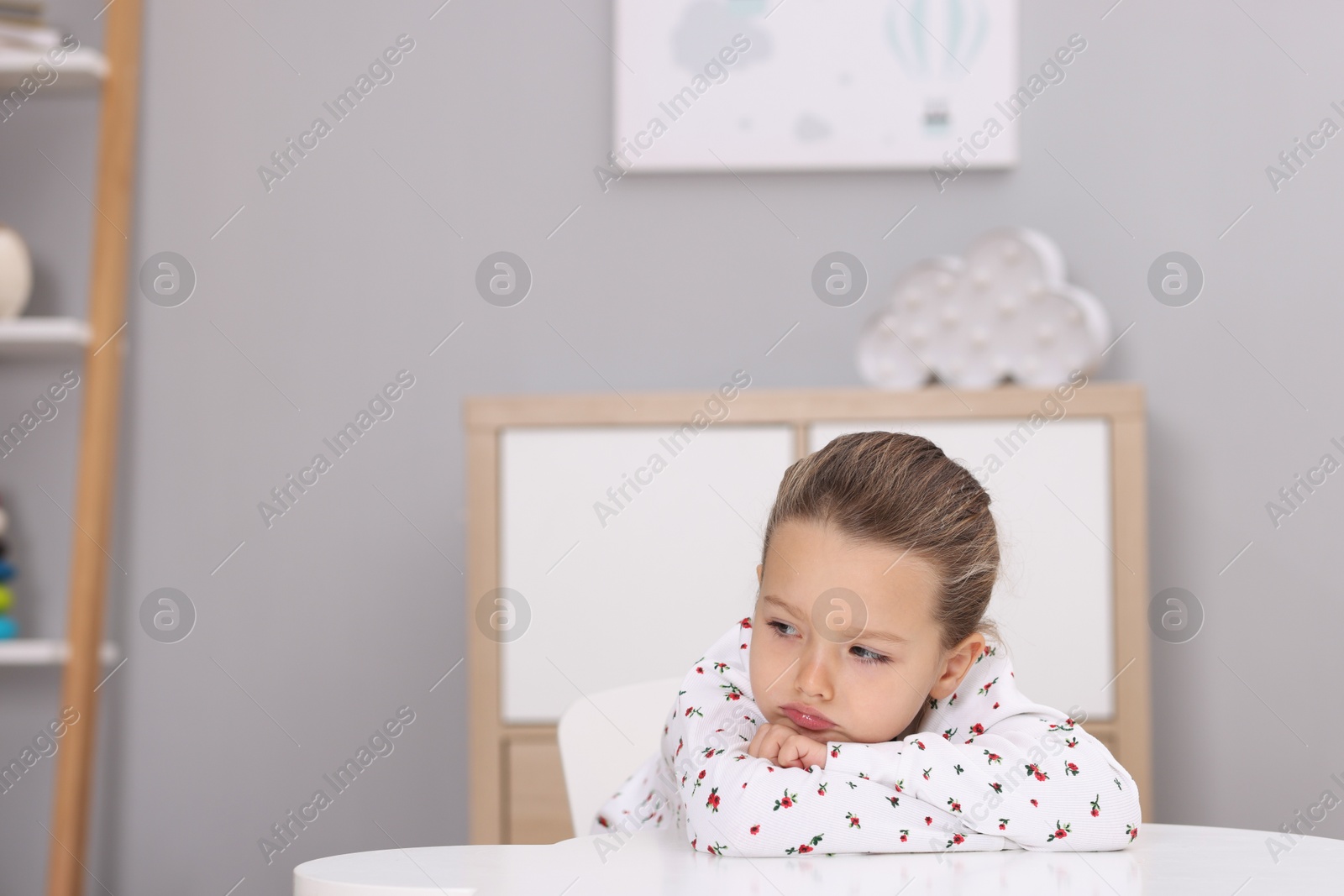 Photo of Resentful little girl at white table indoors, space for text