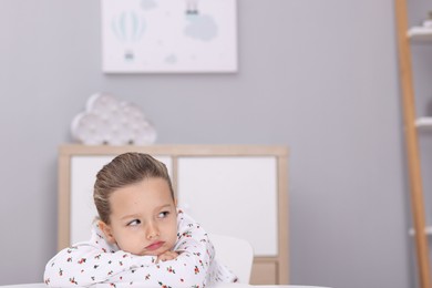 Photo of Resentful little girl at white table indoors, space for text