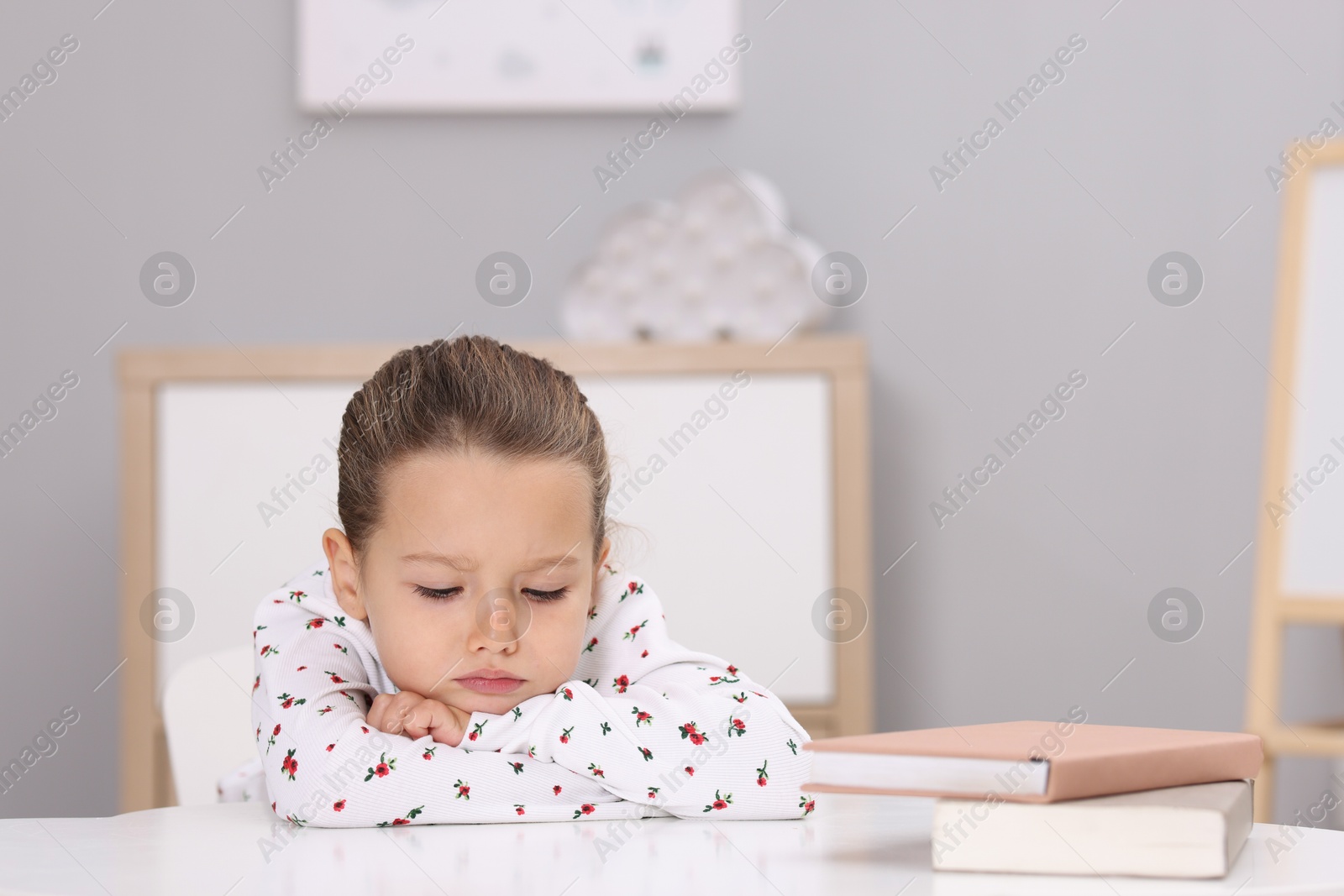 Photo of Resentful little girl at white table indoors, space for text