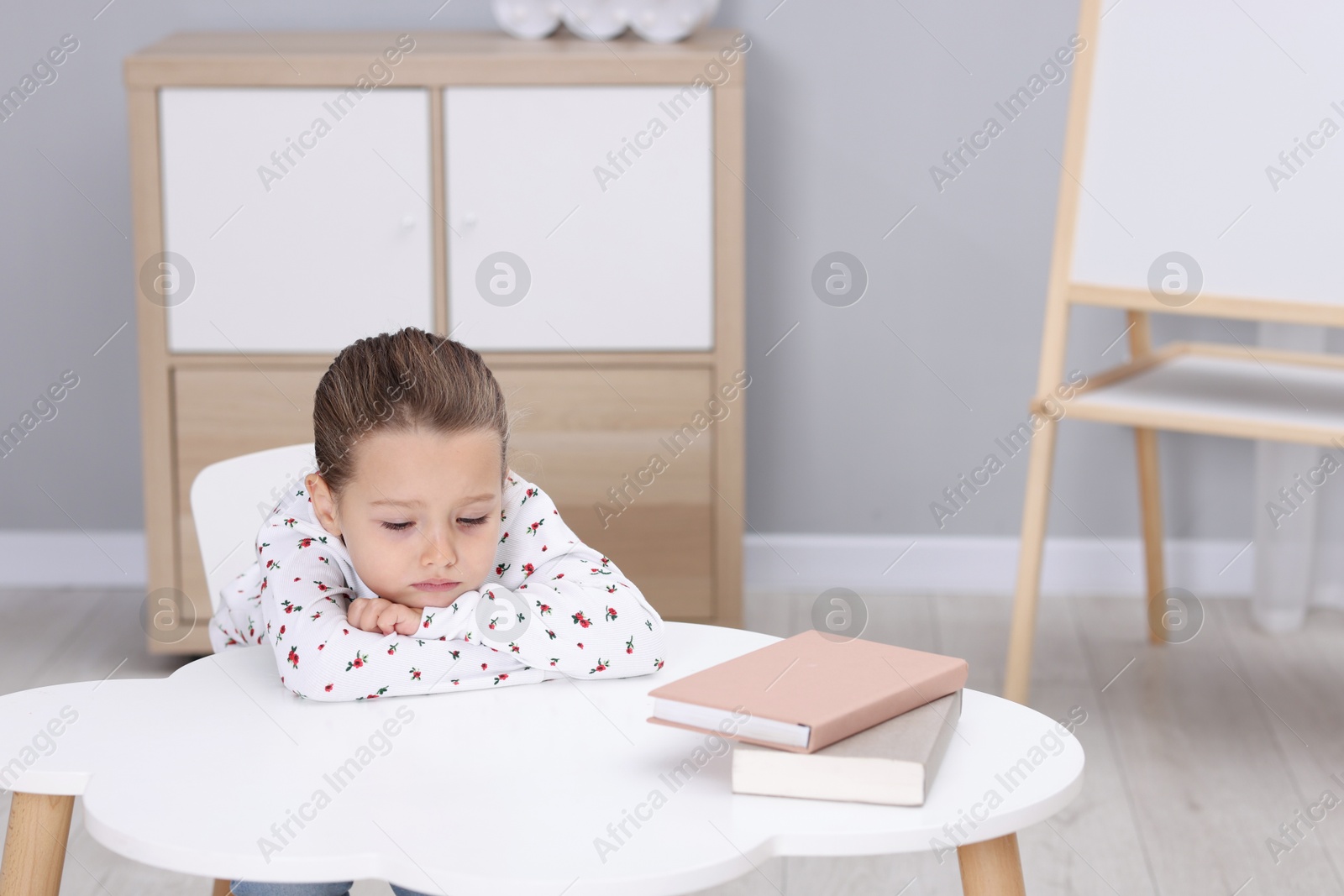 Photo of Resentful little girl at white table indoors, space for text