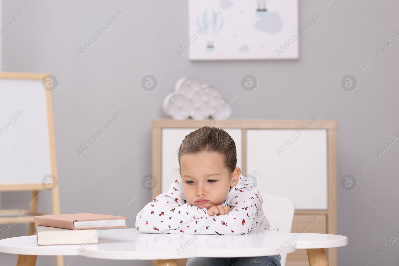 Photo of Resentful little girl at white table indoors