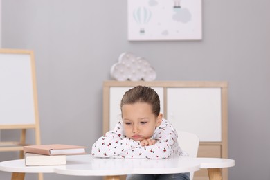 Photo of Resentful little girl at white table indoors