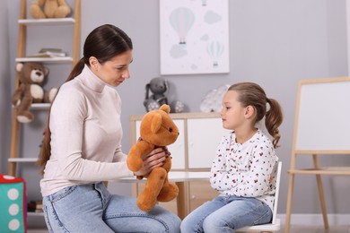 Photo of Resentful little girl and her mother with teddy bear at home. Family dispute