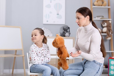 Photo of Resentful little girl and her mother with teddy bear at home. Family dispute