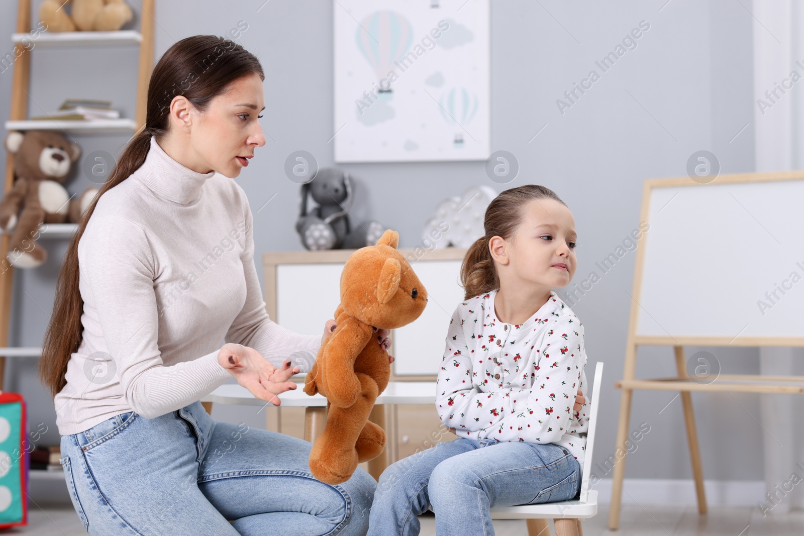 Photo of Resentful little girl and her mother with teddy bear at home. Family dispute