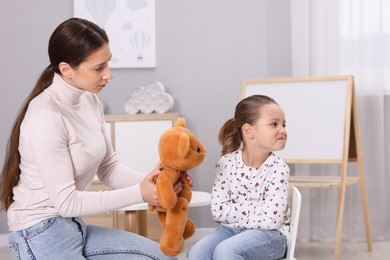 Photo of Resentful little girl and her mother with teddy bear at home. Family dispute