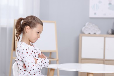 Photo of Resentful little girl at white table indoors, space for text