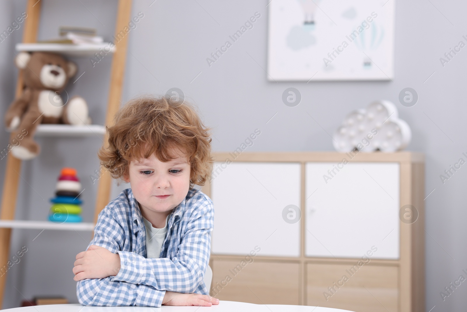 Photo of Resentful little boy at white table indoors, space for text