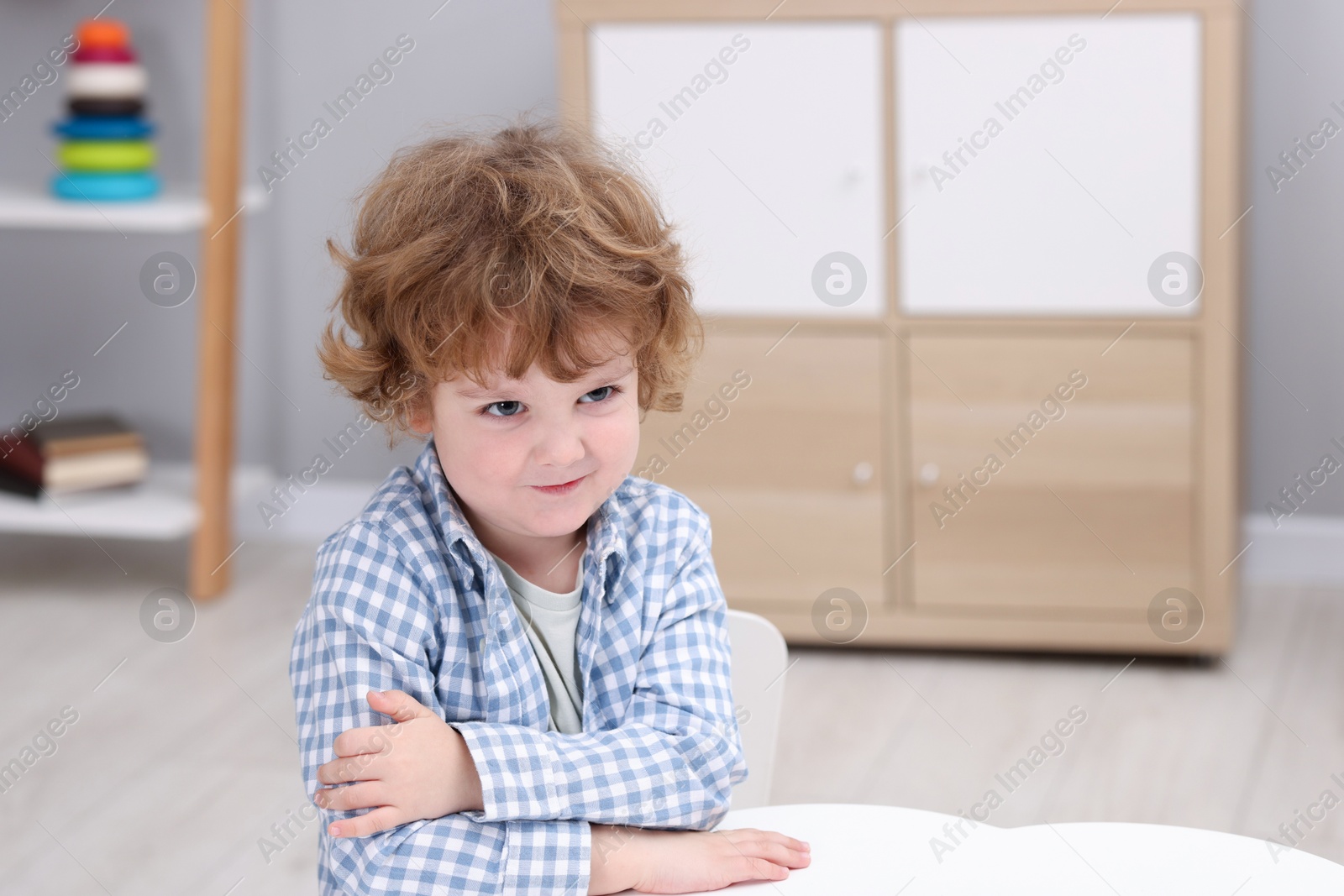 Photo of Resentful little boy at white table indoors, space for text