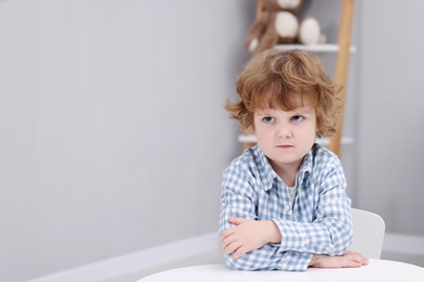 Resentful little boy at white table indoors, space for text