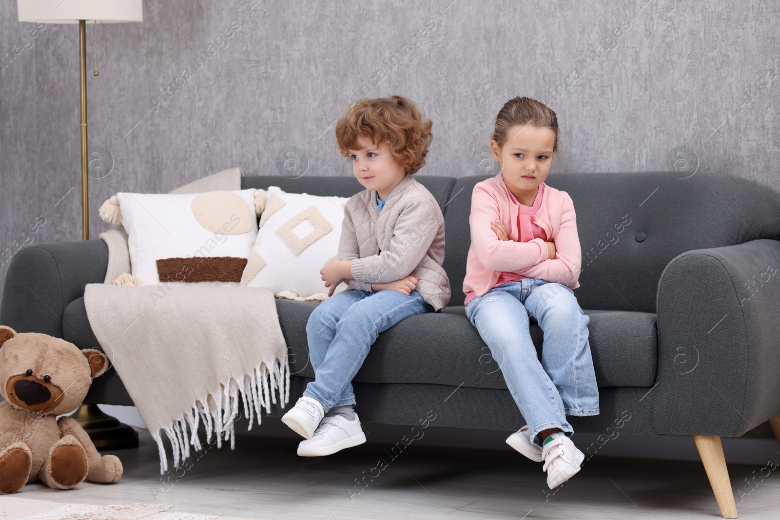 Photo of Resentful little brother and sister on couch at home. Family dispute