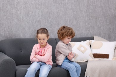 Photo of Resentful little brother and sister on couch at home. Family dispute