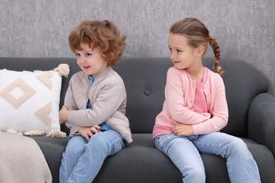 Photo of Resentful little brother and sister on couch at home. Family dispute