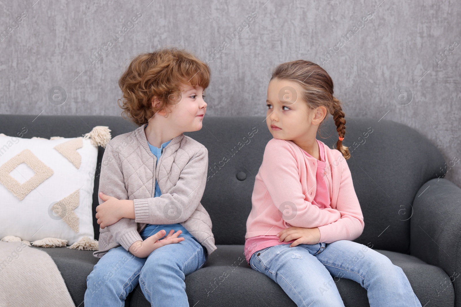 Photo of Resentful little brother and sister on couch at home. Family dispute