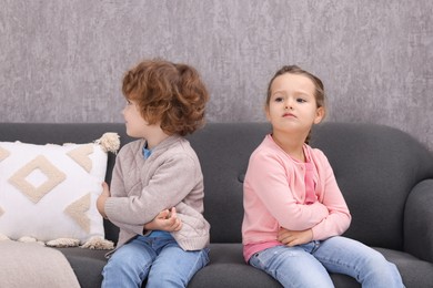 Photo of Resentful little brother and sister on couch at home. Family dispute