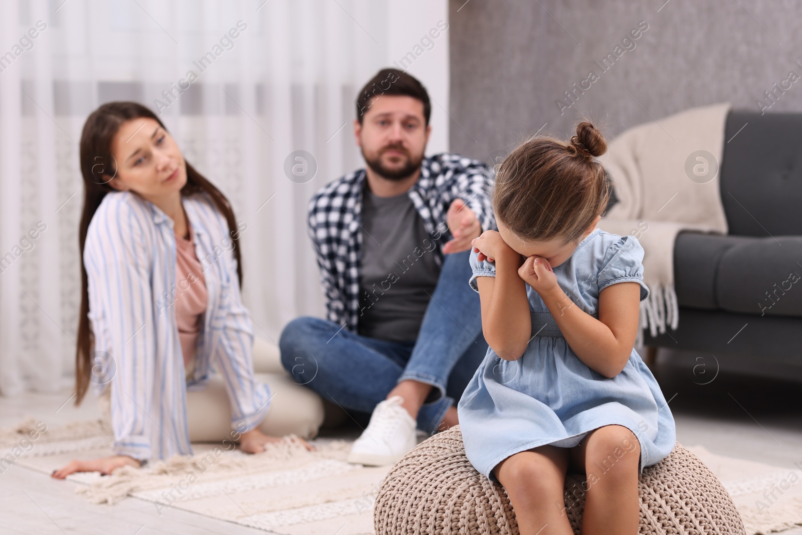 Photo of Resentful little girl crying near her parents at home. Family dispute