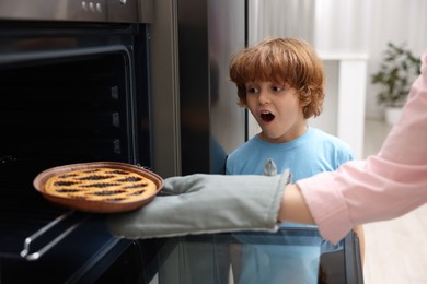 Photo of Mother and her emotional son taking out pie from oven in kitchen, closeup