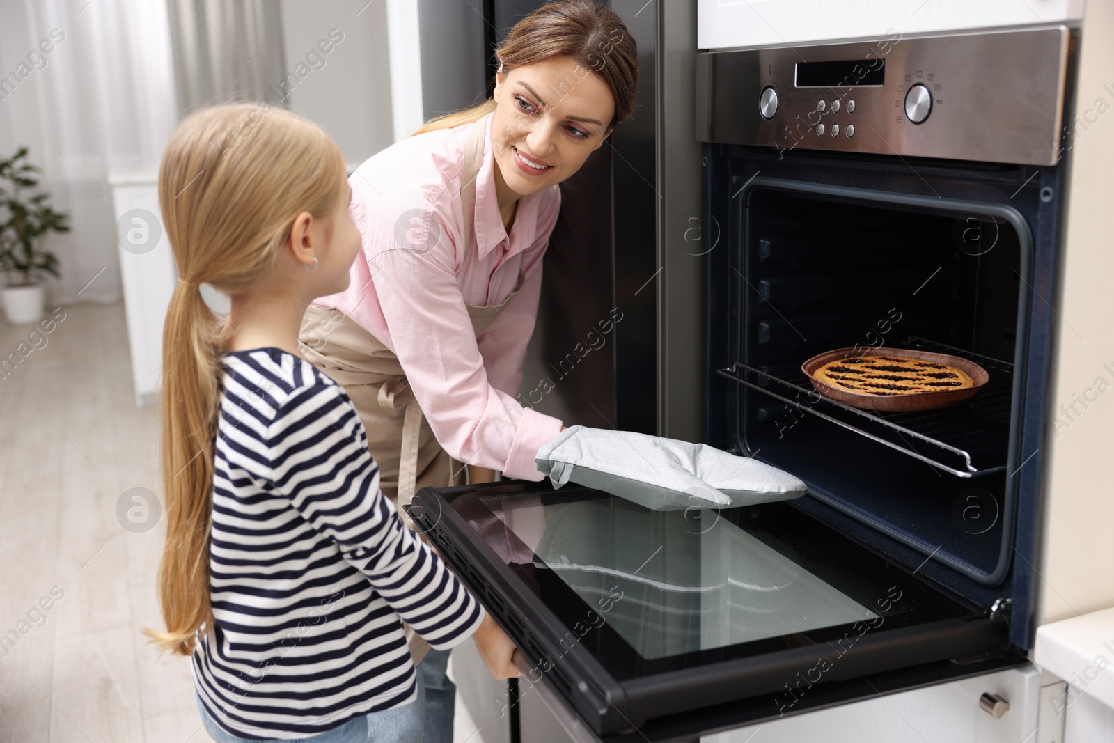 Photo of Mother and her daughter taking out pie from oven in kitchen