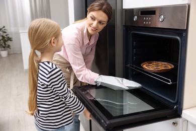 Photo of Mother and her daughter taking out pie from oven in kitchen