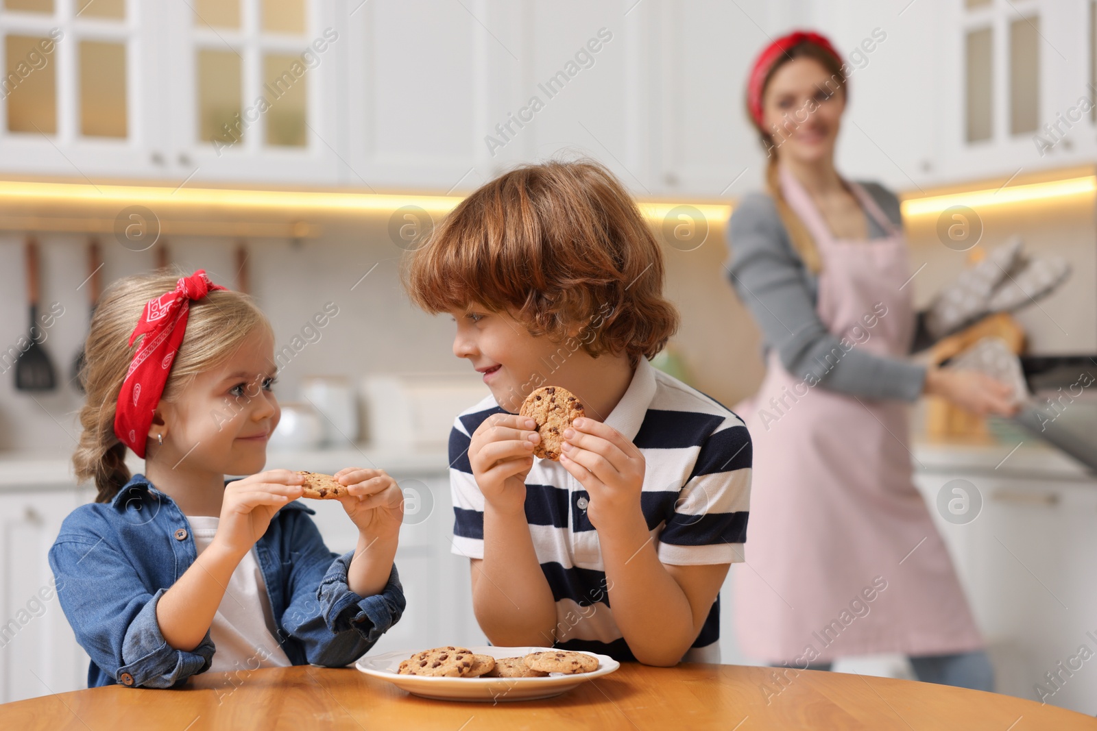 Photo of Happy kids eating tasty cookies while their mother baking in kitchen, selective focus