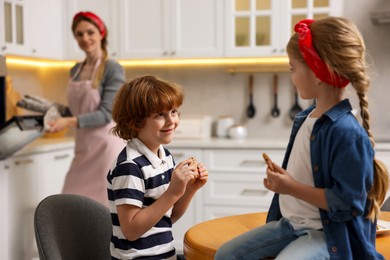 Photo of Happy kids eating tasty cookies while their mother baking in kitchen, selective focus