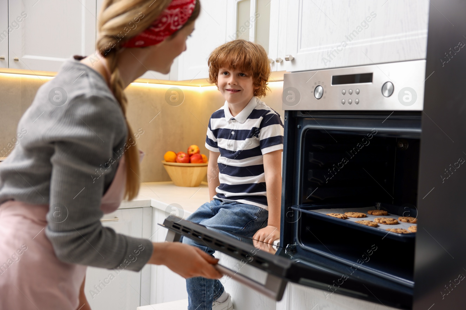 Photo of Mother and her son baking cookies in oven indoors