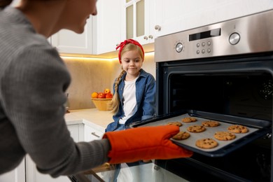 Photo of Mother and her daughter taking out buns from oven in kitchen, closeup