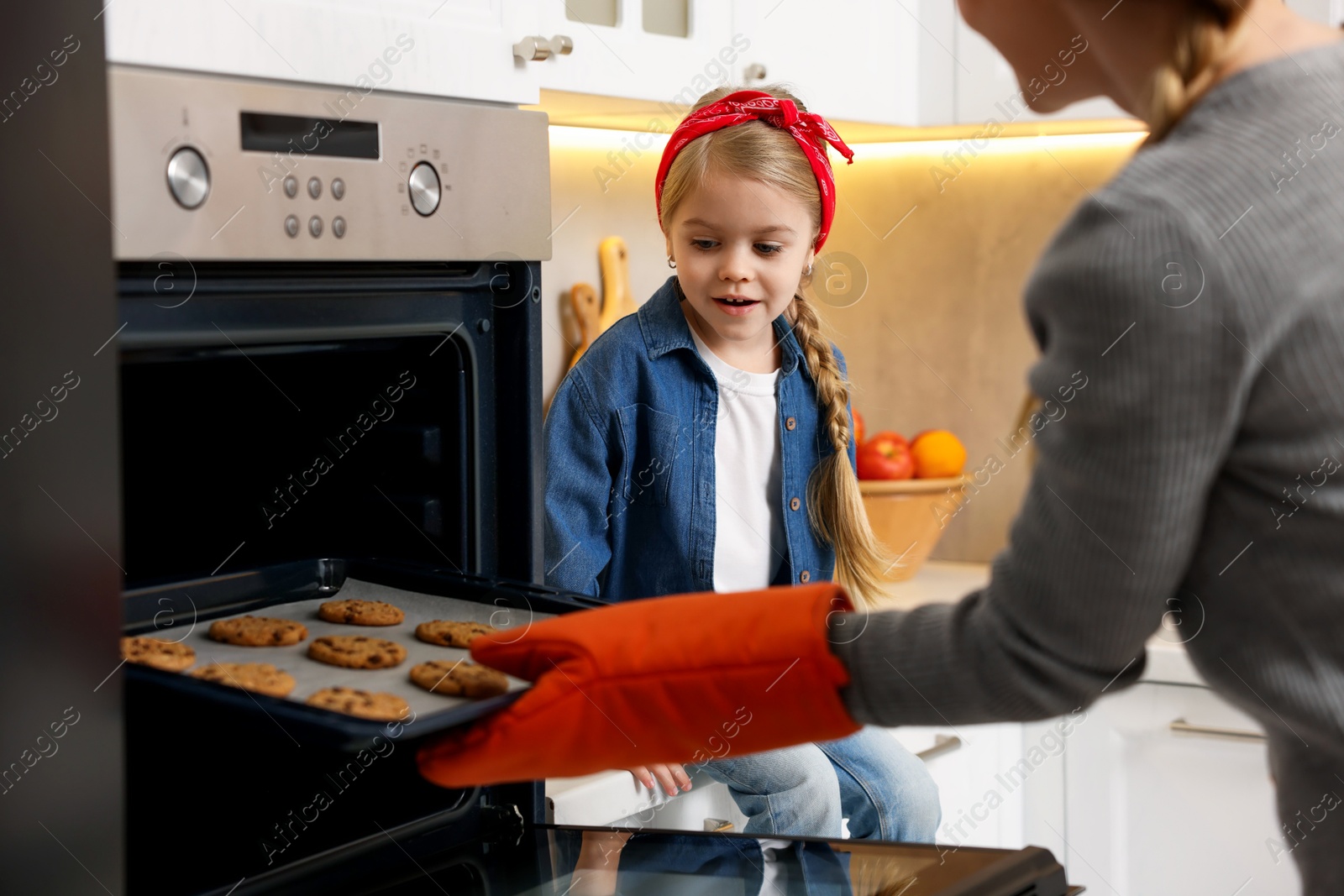 Photo of Mother and her daughter taking out buns from oven in kitchen, closeup