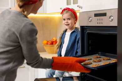 Photo of Mother and her daughter taking out buns from oven in kitchen, closeup