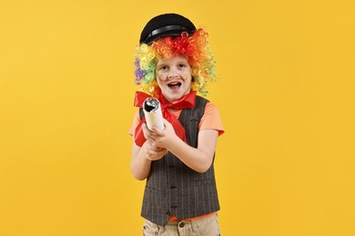 Photo of Happy little boy dressed like clown with confetti popper on yellow background. Surprise party