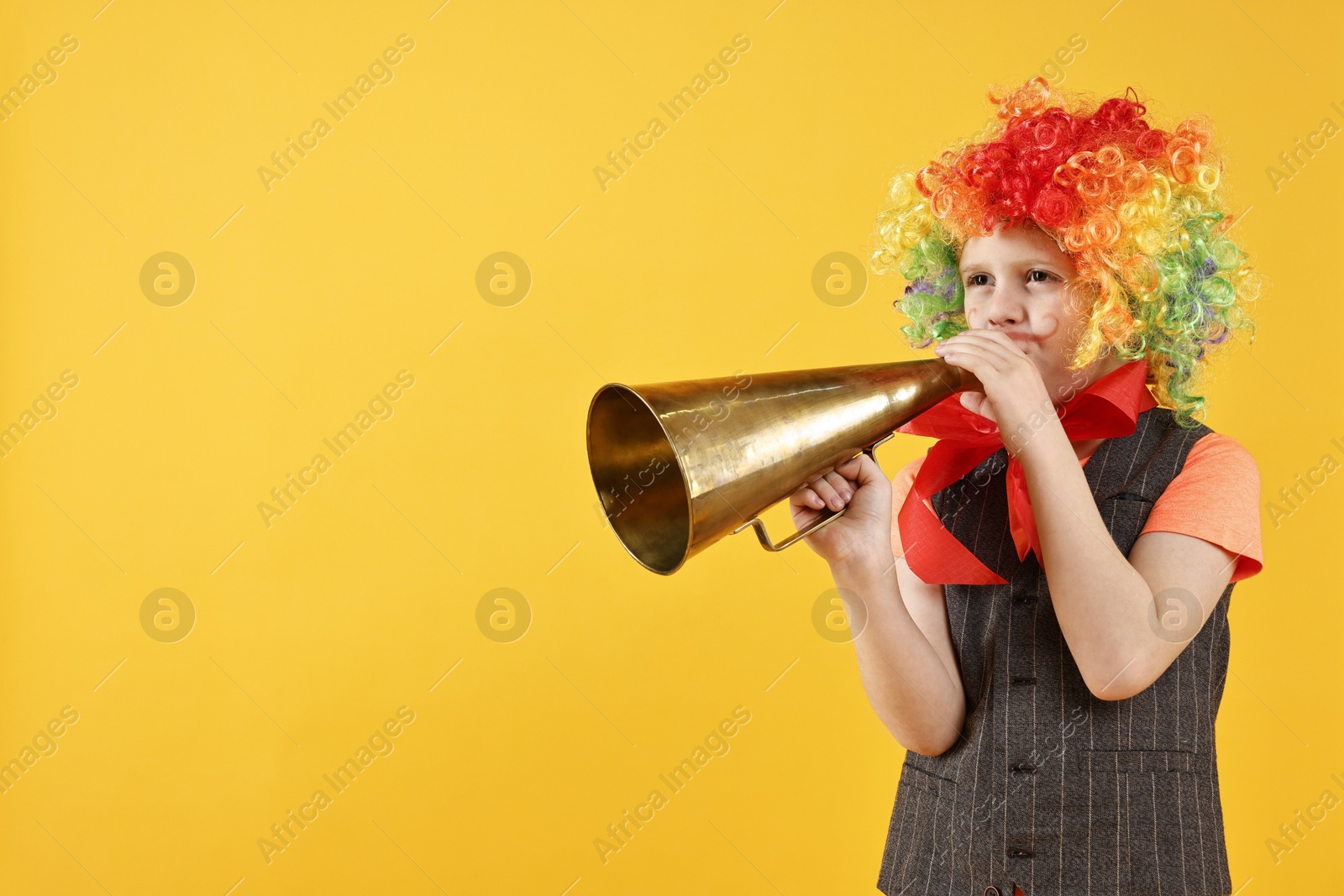 Photo of Little boy dressed like clown with megaphone on yellow background, space for text. Surprise party