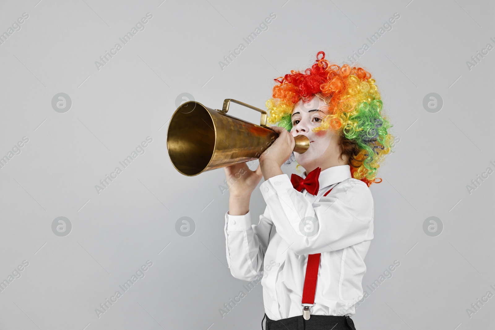 Photo of Little boy dressed like clown with megaphone on grey background, space for text. Surprise party