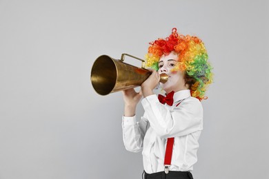 Photo of Little boy dressed like clown with megaphone on grey background, space for text. Surprise party