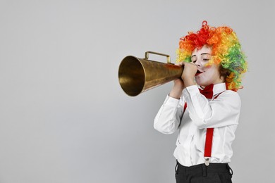 Photo of Little boy dressed like clown with megaphone on grey background, space for text. Surprise party