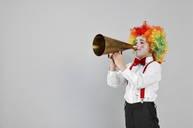 Photo of Little boy dressed like clown with megaphone on grey background, space for text. Surprise party