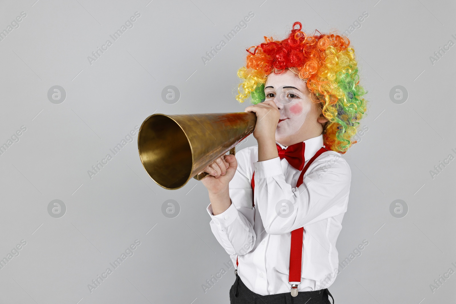 Photo of Little boy dressed like clown with megaphone on grey background, space for text. Surprise party