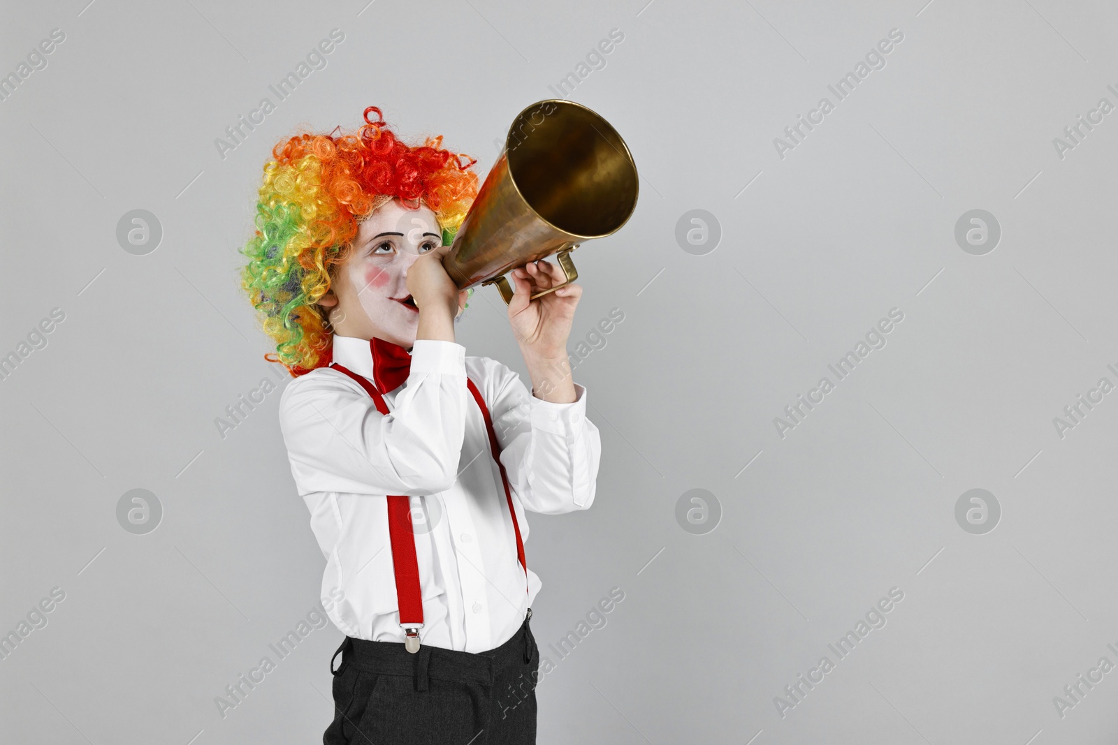 Photo of Little boy dressed like clown with megaphone on grey background, space for text. Surprise party