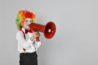 Photo of Little boy dressed like clown with megaphone on grey background, space for text. Surprise party