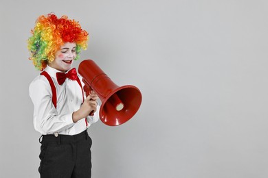 Photo of Happy little boy dressed like clown with megaphone on grey background, space for text. Surprise party