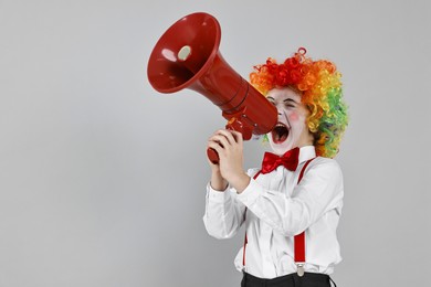 Photo of Little boy dressed like clown shouting in megaphone on grey background, space for text. Surprise party