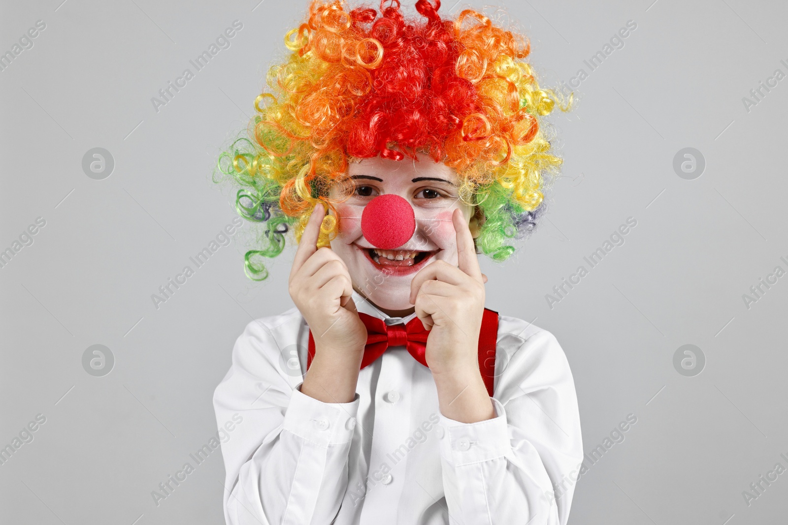 Photo of Happy little boy in clown wig and red nose on grey background. Surprise party