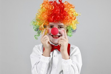 Photo of Happy little boy in clown wig and red nose on grey background. Surprise party