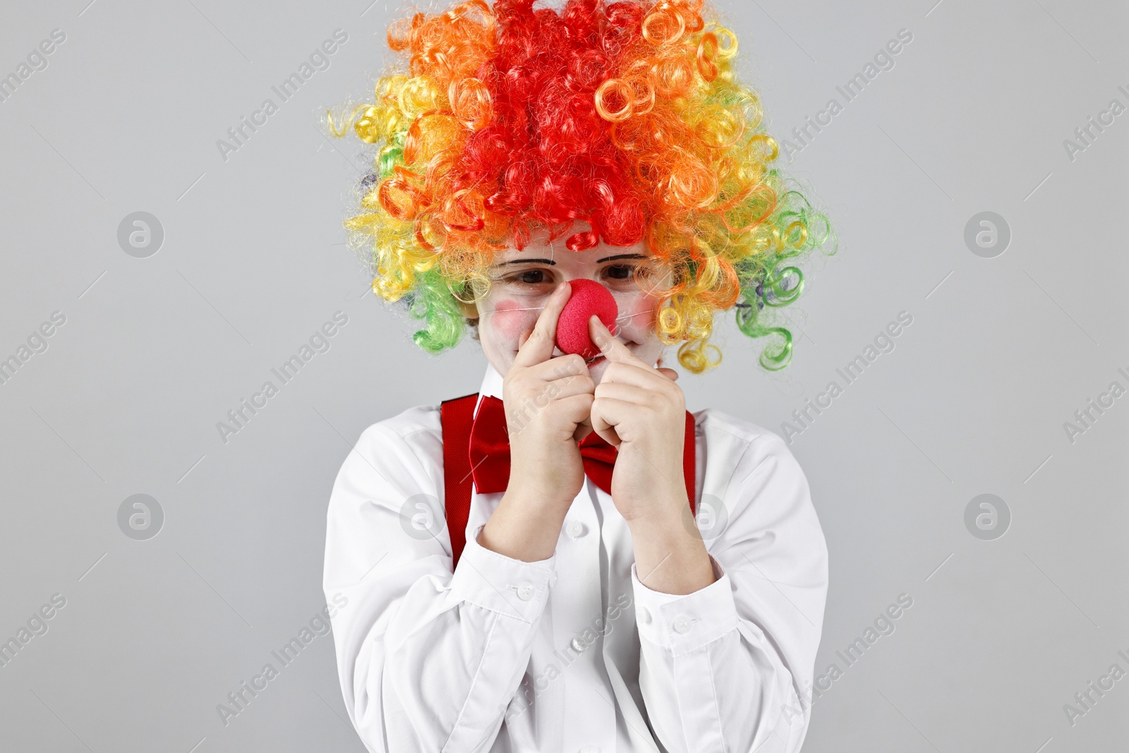 Photo of Cute little boy in clown wig and red nose on grey background. Surprise party