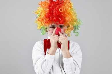 Photo of Cute little boy in clown wig and red nose on grey background. Surprise party