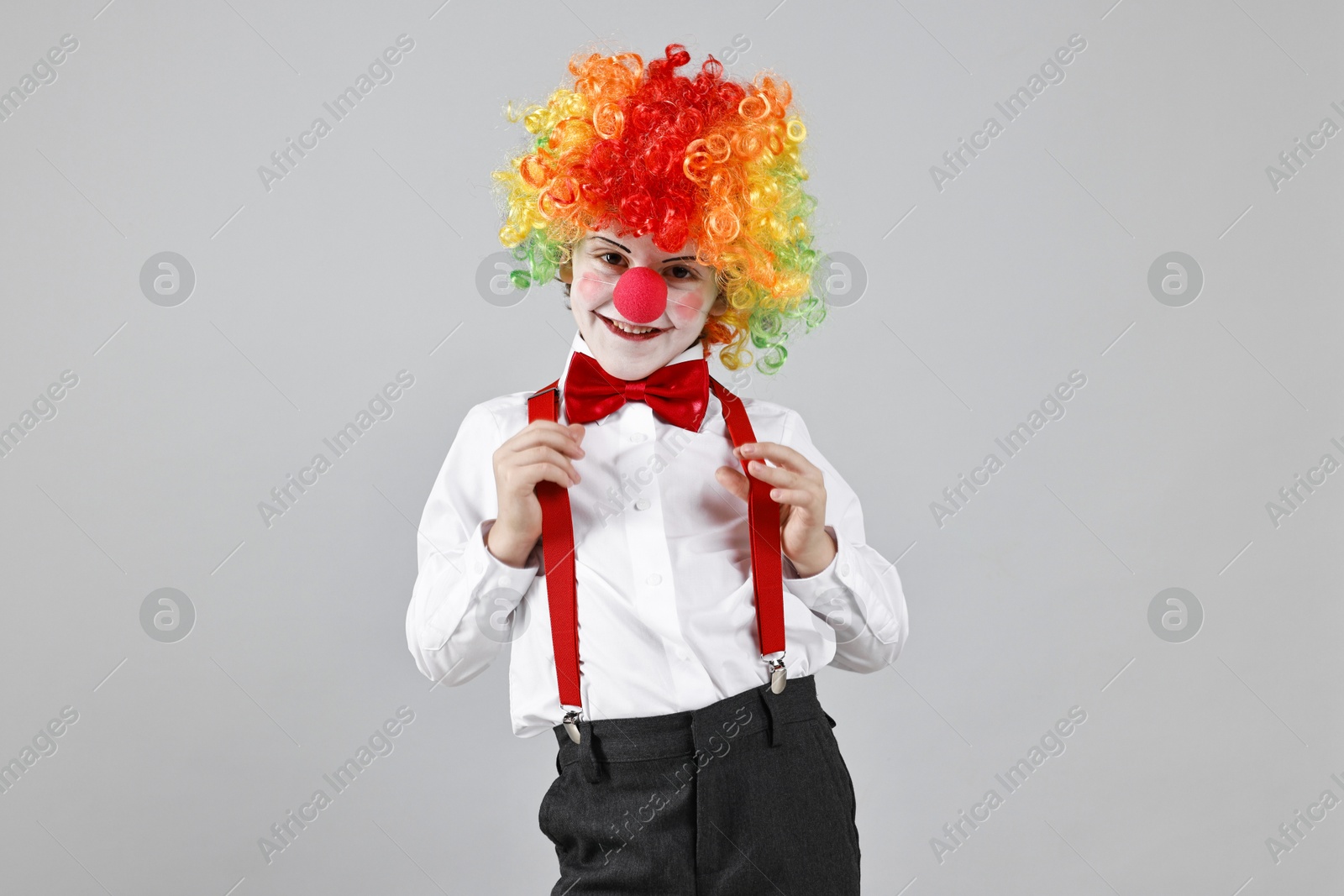 Photo of Happy little boy in clown wig and red nose on grey background. Surprise party