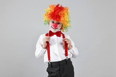 Photo of Happy little boy in clown wig and red nose on grey background. Surprise party